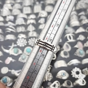May include: A silver ring with a geometric design, measured on a ring sizer, showing a size 9.