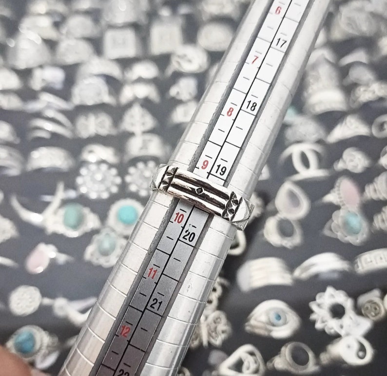 May include: A silver ring with a geometric design, measured on a ring sizer, showing a size 9.