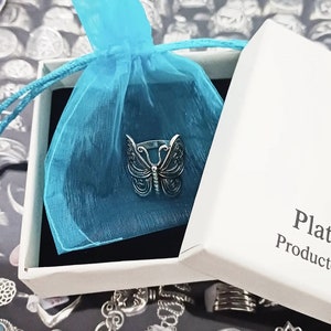 Puede incluir: Un anillo de mariposa de plata en una caja blanca con una bolsa de tul azul. La caja tiene el texto "Plata" y "Producto" impreso en ella.
