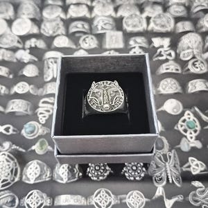 Könnte beinhalten: Ein silberner Ring mit detailliertem Wolfskopf-Design, präsentiert in einer grauen Schachtel. Der Ring weist komplizierte Muster auf und ist von einer Sammlung anderer Silberringe mit verschiedenen Designs umgeben.
