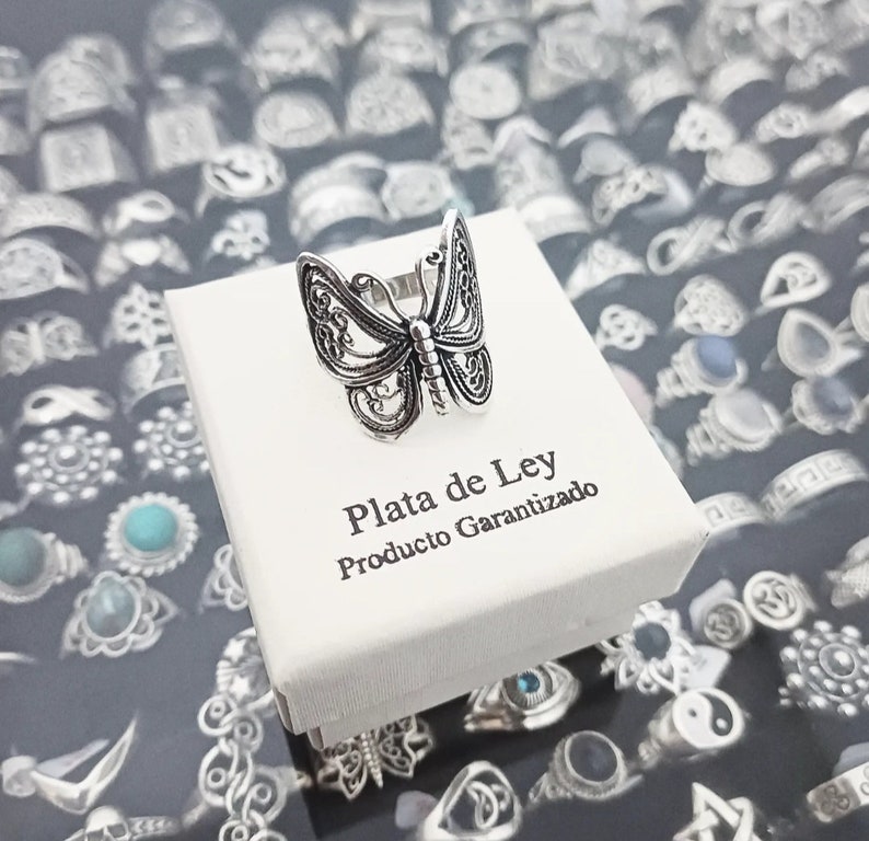 Puede incluir: Un anillo de plata en forma de mariposa en una caja blanca con el texto "Plata de Ley Producto Garantizado".