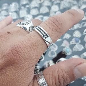 May include: A silver ring with a geometric design. The ring is worn on a person's finger.