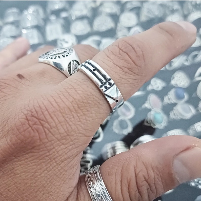 May include: A silver ring with a geometric design. The ring is worn on a person's finger.