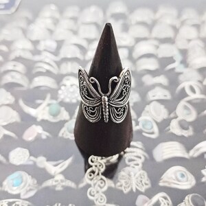 Puede incluir: Un anillo de mariposa de plata en un expositor de madera negro. El anillo est&aacute; rodeado de muchos otros anillos de plata.
