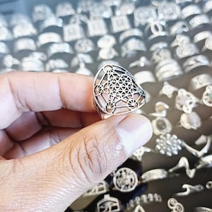 May include: A silver ring featuring a geometric design. The ring is triangular in shape and has a detailed pattern of overlapping circles and lines.