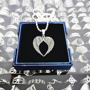 May include: A silver necklace with a heart-shaped pendant featuring angel wings. The necklace is displayed in a blue velvet jewelry box.