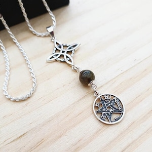 Peut inclure: Collier pendentif argenté avec un pentagramme dans un cercle, un motif de trèfle à quatre feuilles et une pierre précieuse vert foncé. La chaîne a une texture de corde. Le collier est présenté sur une surface en bois clair.