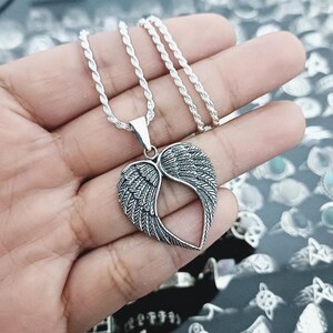 May include: A silver chain necklace with a pendant featuring a heart-shaped design with angel wings. The wings are detailed with intricate lines and have a textured finish.