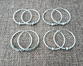 May include: Four silver hoop earrings arranged in two rows. Each pair features distinct decorative metal accents, including textured bands, small spherical beads, and intricate etched patterns along the lower sections of the circular wire frames.