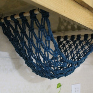 May include: A teal blue macrame hammock hanging from a wooden shelf. The hammock is made of knotted rope and is designed to hold small items.