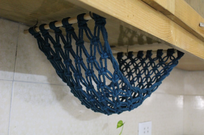 May include: A teal blue macrame hammock hanging from a wooden shelf. The hammock is made of knotted rope and is designed to hold small items.