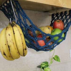 May include: A blue hanging fruit hammock with bananas, apples, and mangoes. The hammock is made of rope and is hanging from a wooden shelf.