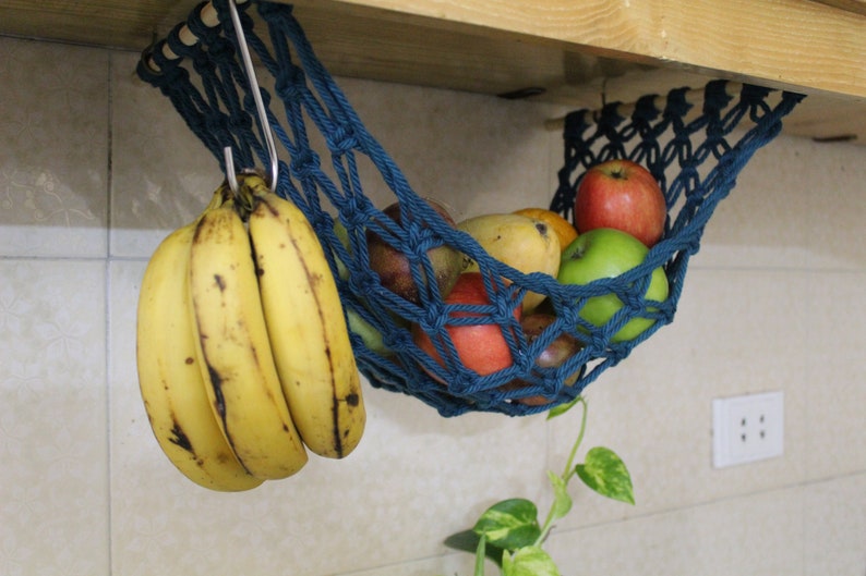 May include: A blue hanging fruit hammock with bananas, apples, and mangoes. The hammock is made of rope and is hanging from a wooden shelf.