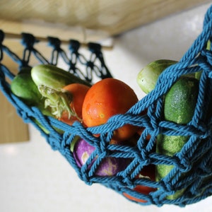 May include: A teal blue rope hammock hanging from a wooden shelf, filled with fresh produce, including cucumbers, tomatoes, and a purple eggplant.
