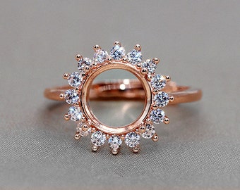 May include: A rose gold ring with a round bezel setting surrounded by a halo of small clear stones.