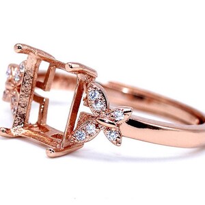 May include: Rose gold ring with a square setting and butterfly accents. The ring is adorned with small clear stones.