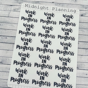 Può includere: Un foglio di adesivi per planner con la scritta "Work in Progress" in stile scritto a mano. Gli adesivi neri su sfondo bianco sono disposti in un motivo ripetuto. Il marchio "Midnight Planning" è in alto.