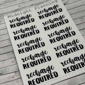 Op de afbeelding: Een vel stickers met de tekst "recharge required" negen keer herhaald in zwarte cursieve letters op een witte achtergrond. De stickers zijn gerangschikt in drie rijen van drie. Het vel is in de linkerbovenhoek geëtiketteerd met "Midnight Planning".