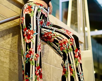 May include: A woman wearing a black crop top and black and white striped pants with a floral print. The pants are wide-legged and flowy.