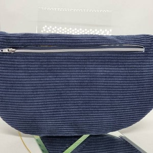May include: A dark blue corduroy fanny pack with a silver zipper and a silver ring on the strap.