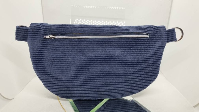 May include: A dark blue corduroy fanny pack with a silver zipper and a silver ring on the strap.