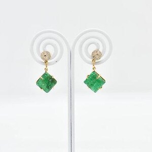 Könnte beinhalten: Ein Paar goldfarbene Hängeohrringe. Jeder Ohrring hat einen kleinen, runden, diamantbesetzten Stecker und einen quadratischen, smaragdgrünen Edelstein. Die Ohrringe werden auf einem weißen Ständer vor weißem Hintergrund präsentiert.