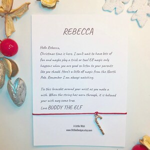 Peut inclure: Bracelet en cordon rouge avec un charme en forme de canne en sucre dorée. La carte attachée au bracelet contient un message pour Rebecca de la part de Buddy l'elfe. Le message dit : "C'est Noël ! J'ai hâte de m'amuser et peut-être de faire une ou deux farces ! La magie des elfes ne fonctionne que lorsque vous êtes bien élevé, alors écoutez vos parents comme vous devriez. Voici un peu de magie d'elfe du pôle Nord. N'oubliez pas que je vous surveille toujours. Attachez ce bracelet autour de votre poignet lorsque vous faites un vœu. Lorsque le cordon sera usé, on dit que votre vœu se réalisera. Avec amour, Buddy l'elfe."