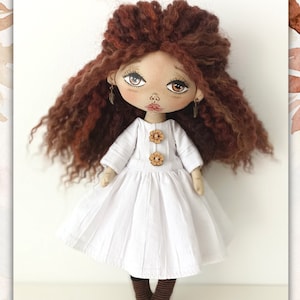 May include: A handmade doll with long, curly brown hair, wearing a white dress with brown buttons and brown socks. The doll has a painted face with brown eyes and a pink nose.