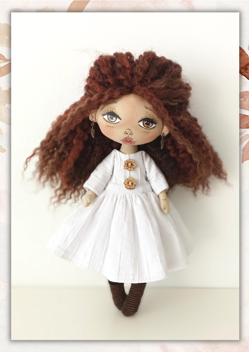 May include: A handmade doll with long, curly brown hair, wearing a white dress with brown buttons and brown socks. The doll has a painted face with brown eyes and a pink nose.