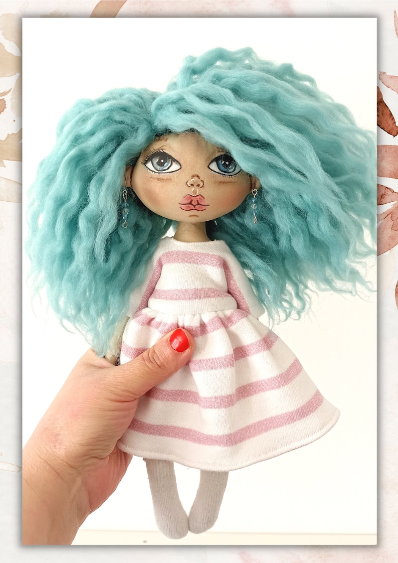 May include: A handmade doll with blue curly hair, wearing a pink and white striped dress and white socks. The doll has painted blue eyes, a pink nose, and red lips.