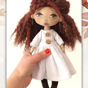 May include: A handmade doll with long, curly red hair, wearing a white dress with wooden flower buttons and brown and white striped socks.