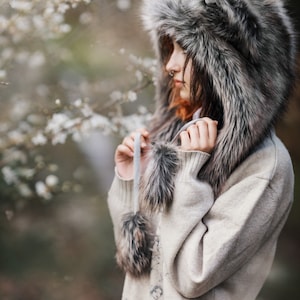 Puede incluir: Un gorro de lobo de piel sint&eacute;tica gris y marr&oacute;n y un su&eacute;ter beige claro. El gorro tiene orejas puntiagudas y el su&eacute;ter tiene un dise&ntilde;o detallado en la espalda. El gorro tiene dos pompones colgantes. Ideal para el invierno.