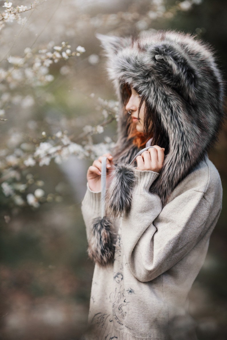 Puede incluir: Un gorro de lobo de piel sint&eacute;tica gris y marr&oacute;n y un su&eacute;ter beige claro. El gorro tiene orejas puntiagudas y el su&eacute;ter tiene un dise&ntilde;o detallado en la espalda. El gorro tiene dos pompones colgantes. Ideal para el invierno.