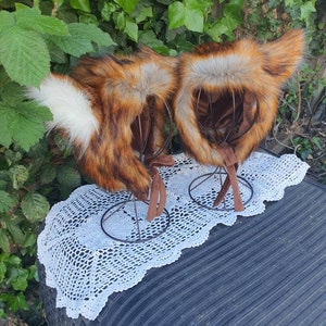 May include: Two fox headbands with brown, orange, and white fur. The headbands are on display stands and have brown ties.