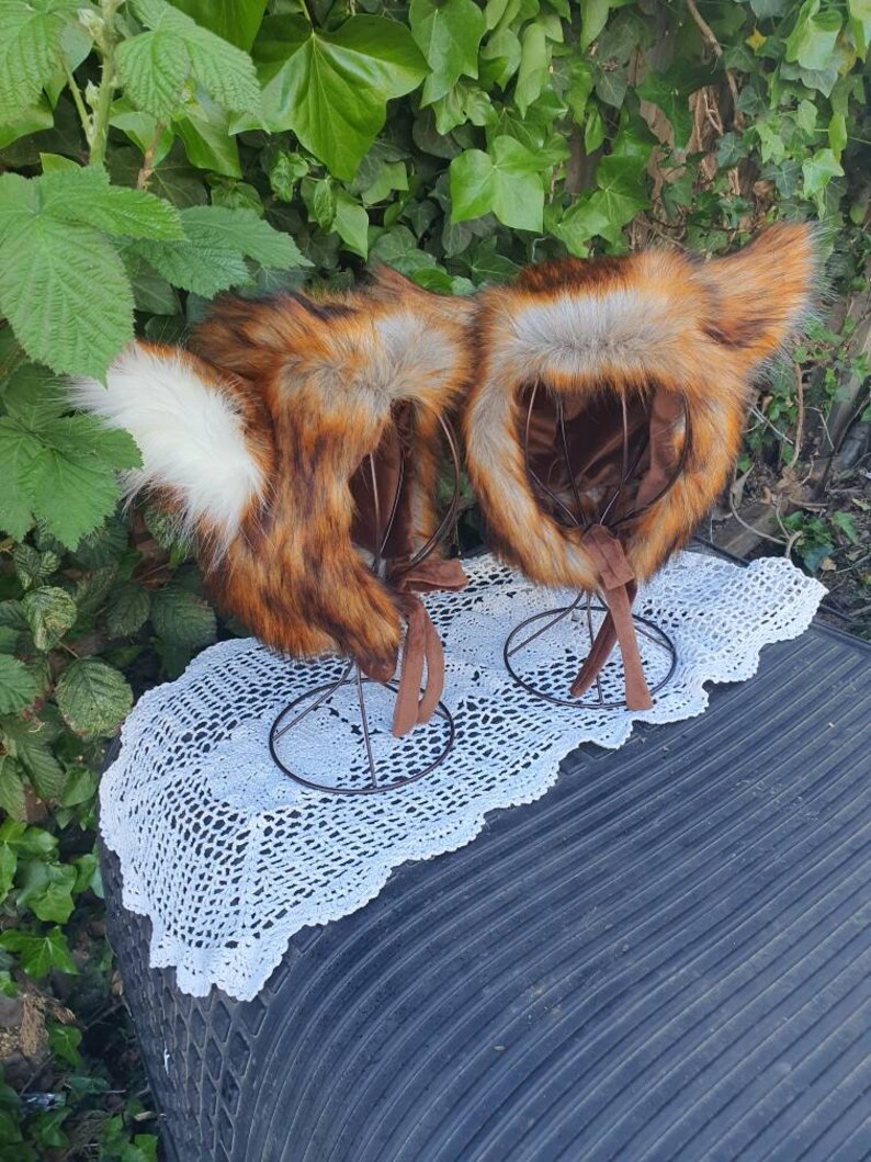 May include: Two fox headbands with brown, orange, and white fur. The headbands are on display stands and have brown ties.