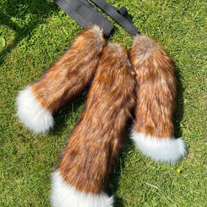 May include: Three brown and white faux fur tails with white tips. The tails are attached to black elastic straps.