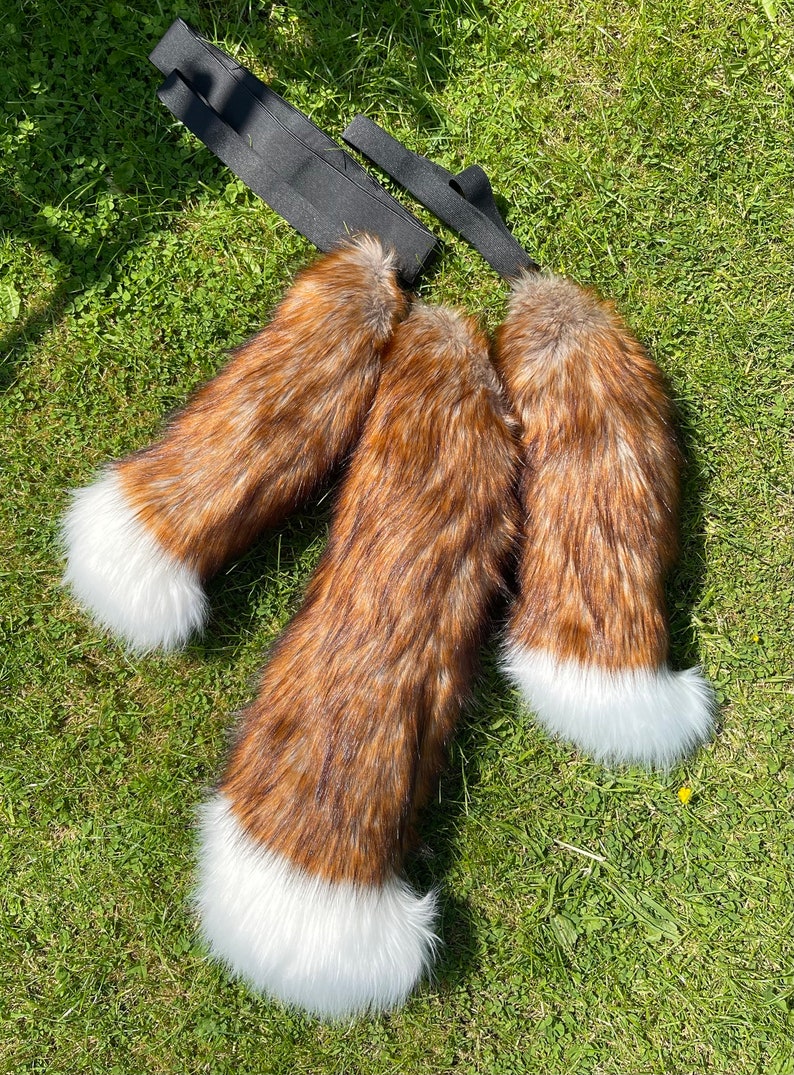May include: Three brown and white faux fur tails with white tips. The tails are attached to black elastic straps.