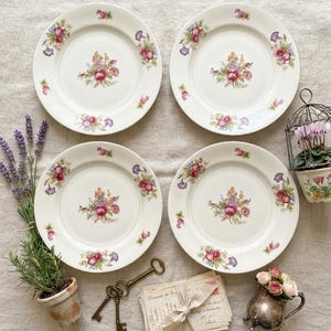 Può includere: Quattro piatti rotondi in ceramica color bianco sporco con un bouquet floreale centrale e piccoli grappoli di fiori lungo il bordo. Il set è accompagnato da una piccola pianta di lavanda, due chiavi in metallo, lettere vintage e una brocca d'argento.
