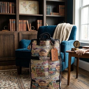 Puede incluir: Un trolley tote de tapiz vintage con un diseño de la Ruta 66, que muestra moteles, coches y el escudo de la Ruta 66. La bolsa tiene un asa negra y una etiqueta de equipaje. El trolley tiene ruedas y está diseñado para viajar.