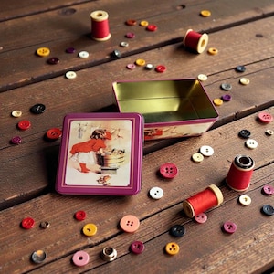 May include: A collection of sewing supplies, including red spools of thread, colorful buttons, and a decorative tin with a vintage illustration. The items are scattered on a wooden surface, creating a charming, nostalgic scene.