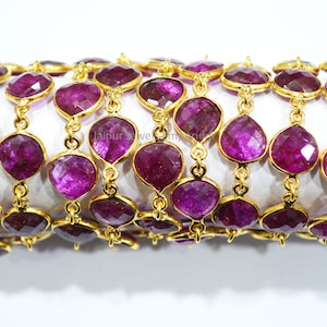 May include: A close-up of a gold chain with faceted purple gemstones. The chain is made of small, round links and the gemstones are set in gold.