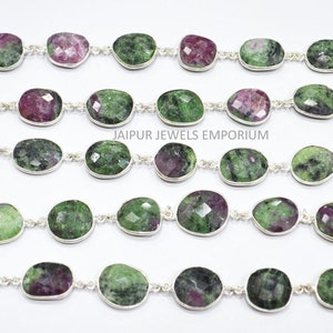 May include: A silver chain necklace featuring green and pink oval-shaped gemstones. The chain is made of small silver links. The gemstones are set in silver bezels. "JAIPUR JEWELS EMPORIUM" is printed on the white background.