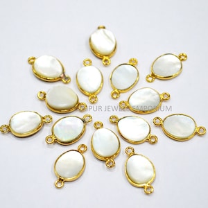 May include: A group of 12 oval-shaped white mother of pearl charms with gold-toned metal accents. Each charm has two jump rings for attaching to jewelry.