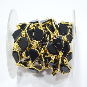 May include: A spool of gemstone chain featuring black, geometric-shaped stones set in gold-colored metal. The chain is tightly wound on a clear plastic spool, ready for use in jewelry making or other crafts.