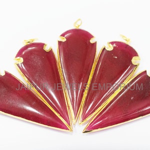 May include: Five red gemstone pendants with gold accents. Each pendant is shaped like a teardrop with a pointed tip. The pendants are arranged in a fan shape.