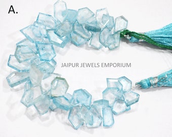 May include: A strand of light blue aquamarine gemstone beads, with a faceted, rectangular shape. The beads are strung on a cord with turquoise tassels at each end. The text "JAIPUR JEWELS EMPORIUM" is printed on a white background.