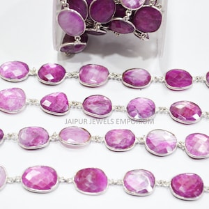 May include: A strand of pink gemstone beads connected by a silver chain. The beads are oval shaped and have a faceted finish. The chain is made of small, round links. The beads and chain are displayed on a white surface.
