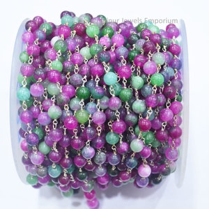 May include: A spool of green and pink gemstone beads strung on a silver chain. The beads are round and have a smooth, polished finish.