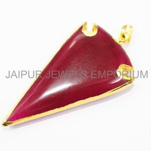May include: A gold-toned pendant with a red gemstone in the shape of a triangle. The pendant has a gold-toned bail for attaching to a chain.
