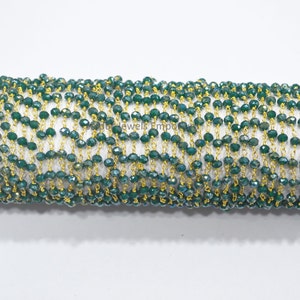 May include: A roll of beaded chain featuring faceted, dark green beads strung on gold-colored wire. The beads have a sparkling, iridescent quality. The chain is tightly wound, showcasing the texture and color of the beads.